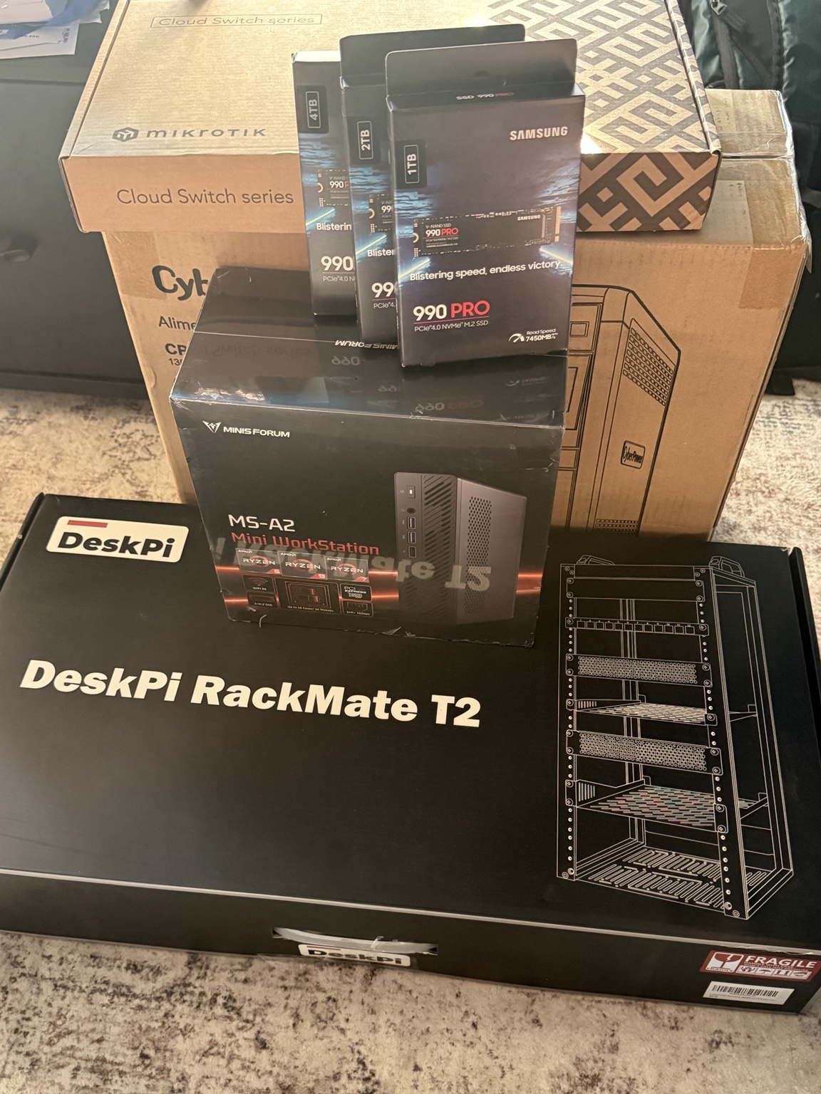 Boxes for the MINISFORUM MS-A2, three Samsung 990 PRO NVMe drives, MikroTik networking, CyberPower UPS, and DeskPi RackMate T2 assembled for the VCF 9.1 home lab